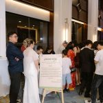 Cô dâu đứng cạnh bảng trưng bày trong không gian tiệc cưới.