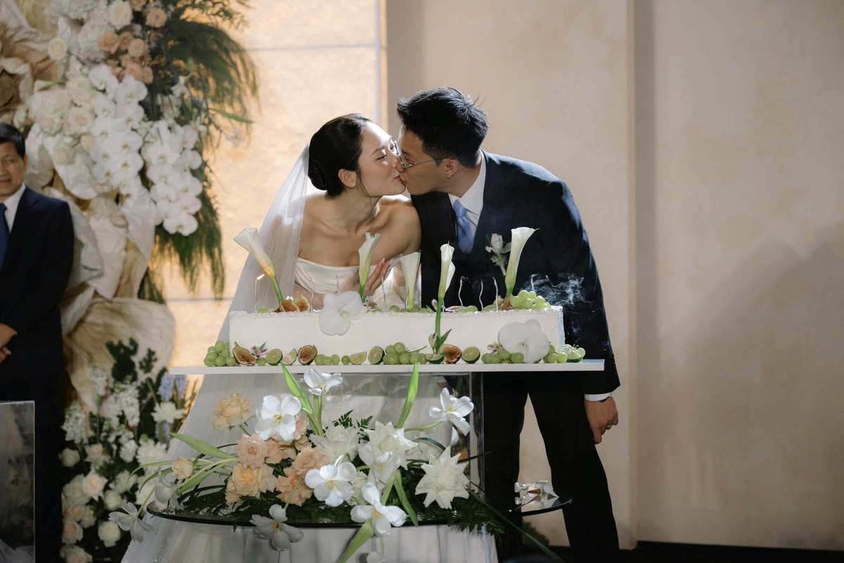 Cô dâu chú rể bên bàn bánh cưới trang trí hoa và nến.